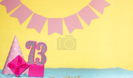 Date of birth for a girl  73. Copy space. Birthday in pink shades with a yellow background. Decorations with numbered candles and a gift box. Anniversary card for a woman