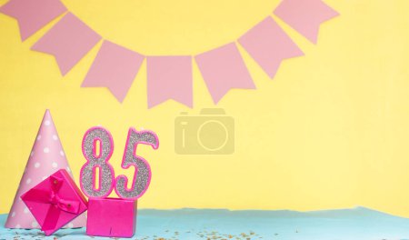 Date of birth for a girl  85. Copy space. Birthday in pink shades with a yellow background. Decorations with numbered candles and a gift box. Anniversary card for a woman