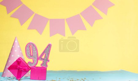 Geburtsdatum eines Mädchens 94. Kopierraum. Geburtstag in Rosatönen vor gelbem Hintergrund. Dekorationen mit nummerierten Kerzen und einer Geschenkbox. Geburtstagskarte für eine Frau