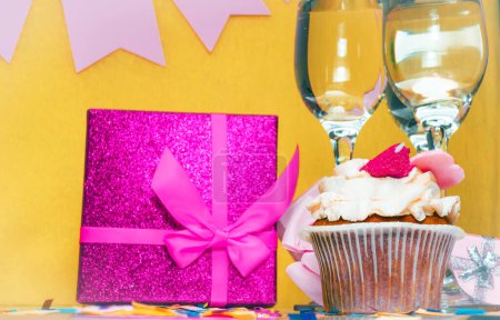 Date of birth with glasses of champagne. Festive pudding pie. Happy birthday decorations for a girl. Gift box with pink bow. Anniversary congratulations, copy space