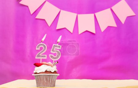 Foto de Fecha de nacimiento con el número 25. Fondo rosa con un pastel y velas encendidas, ahorrar espacio, feliz aniversario de cumpleaños para una chica. Magdalena de pudín de vacaciones. - Imagen libre de derechos