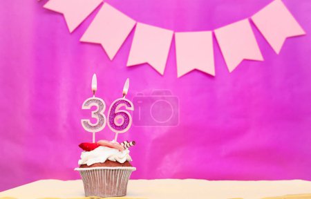 Background date of birth with number  36. Pink background with a cake and burning candles, save space, happy birthday anniversary for a girl. Holiday pudding muffin.