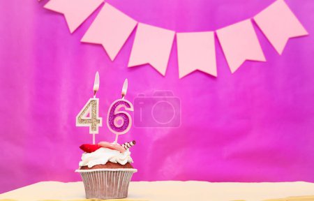 Background date of birth with number  46. Pink background with a cake and burning candles, save space, happy birthday anniversary for a girl. Holiday pudding muffin.