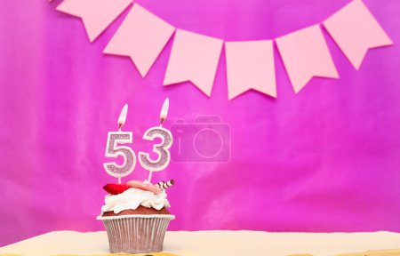 Background date of birth with number  53. Pink background with a cake and burning candles, save space, happy birthday anniversary for a girl. Holiday pudding muffin.