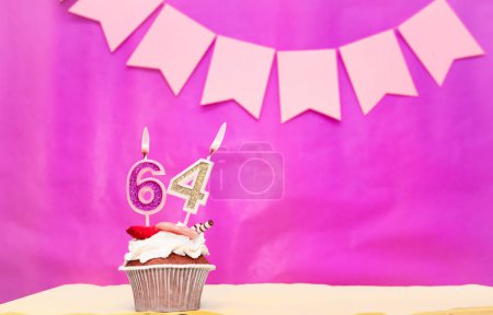 Date de naissance avec le numéro 64. Fond rose avec un gâteau et des bougies allumées, économiser de l'espace, joyeux anniversaire pour une fille. Muffin au pudding de vacances.