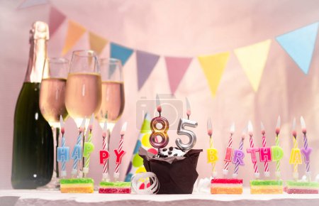 Birthday with champagne and glasses. Birthday candle with number 85. Anniversary card with garlands save space. Festive background.