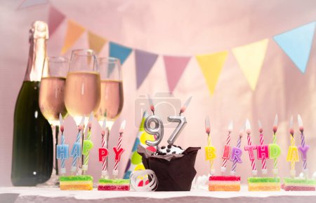 Birthday with champagne and glasses. Birthday candle with number 97. Anniversary card with garlands save space. Festive background.