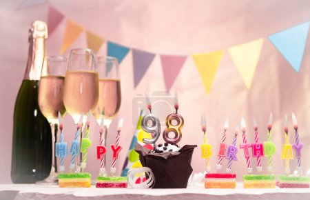 Birthday with champagne and glasses. Birthday candle with number 98. Anniversary card with garlands save space. Festive background.