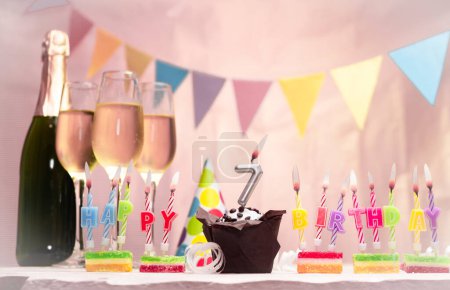 Birthday with champagne and glasses. Birthday candle with number 7. Anniversary card with garlands save space. Festive background.