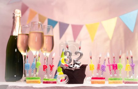 Birthday with champagne and glasses. Birthday candle with number 32. Anniversary card with garlands save space. Festive background.