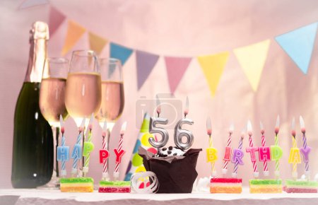 Geburtstag mit Champagner und Gläsern. Geburtstagskerze mit der Nummer 56. Geburtstagskarte mit Girlanden spart Platz. Feierlicher Hintergrund.