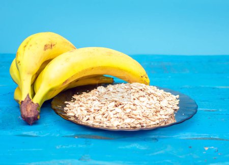 Breakfast, Bananas with oatmeal with fresh milk in a glass. On a blue board, ripe bananas on a blue wooden table.