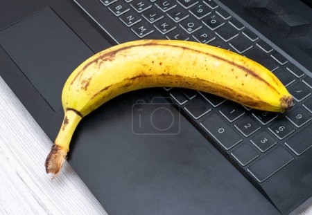 Banane sur la table avec ordinateur portable. Banane sur le bureau du bureau. Banane mûre sur une table en bois
