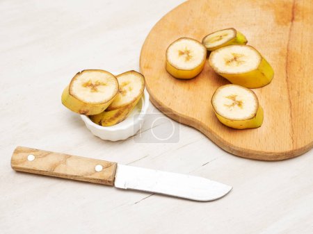 Banane tranchée sur une planche à découper de cuisine avec un couteau.