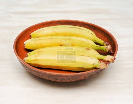 Banana in a clay plate, natural ripe bananas in a plate on the kitchen table.