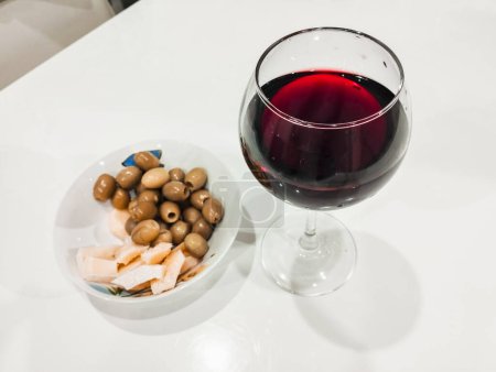 Un verre de vin avec du parmesan et des olives. Vin naturel dans un verre sur la table de cuisine. Boisson alcoolisée rouge.