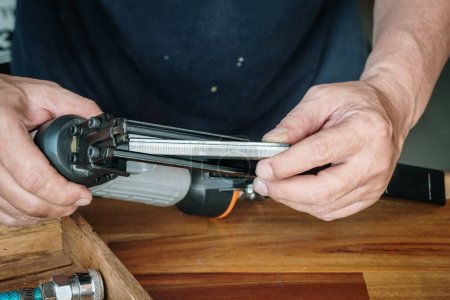 Foto de Carpenter using nail gun or brad nailer tool ,load a top loading stapler  in a workshop ,furniture restoration woodworking concept. selective focus. - Imagen libre de derechos