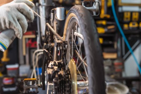 Foto de Mecánico reparación de bicicletas, spray lubricante de cadena para bicicleta plegable trabajando en taller, concepto de reparación y mantenimiento de bicicletas - Imagen libre de derechos