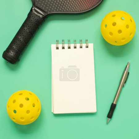 Téléchargez les photos : View from above on pickleballs, racket, pen and white blank notepad on light green background. Square format, with copy space. - en image libre de droit