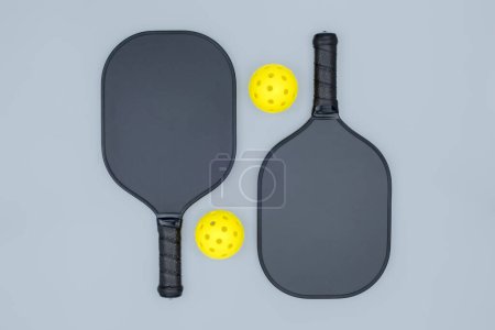 Top view closeup of two pickleball paddles and two yellow balls on light gray background with a copy space