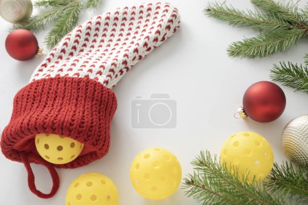 Photo for Close view of a white and red woven Christmas stocking with pickleballs, ornaments and pine branches on white background with copy space. - Royalty Free Image