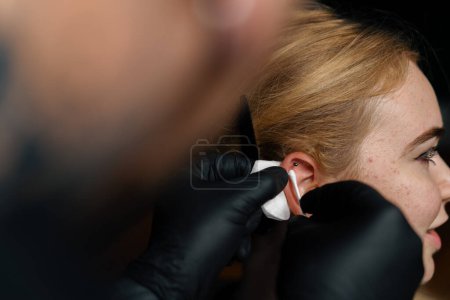 Foto de Estudio de perforación. un maestro perfora la oreja de una chica - Imagen libre de derechos