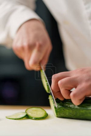 Foto de Chef corta pepino en una tabla de cortar primer plano rebanada de pepino primer plano cocina profesional - Imagen libre de derechos