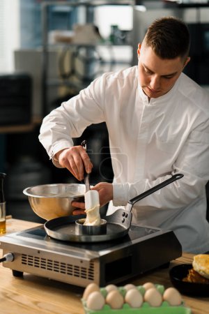 Foto de Un chef profesional en la cocina de un restaurante prepara panqueques para el desayuno. Receta culinaria Sartén en estufa - Imagen libre de derechos