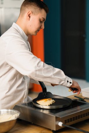 Téléchargez les photos : Un chef professionnel dans la cuisine d'un restaurant prépare des crêpes pour le petit déjeuner. Recette culinaire Poêle sur poêle - en image libre de droit