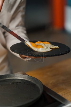 Téléchargez les photos : Délicieux petit déjeuner équilibré et nutritif d'œufs frits sur une assiette noire au restaurant - en image libre de droit