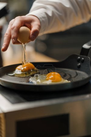 Photo for A cook breaks an egg into a pan Preparing breakfast in professional kitchen - Royalty Free Image