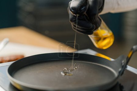 Foto de Un chef vierte aceite en una sartén caliente en una cocina profesional cocinando en un restaurante - Imagen libre de derechos