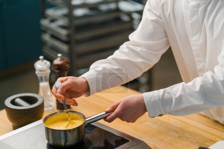Photo for The chef prepares cheese sauce on the stove The work of a professional in restaurant kitchen - Royalty Free Image