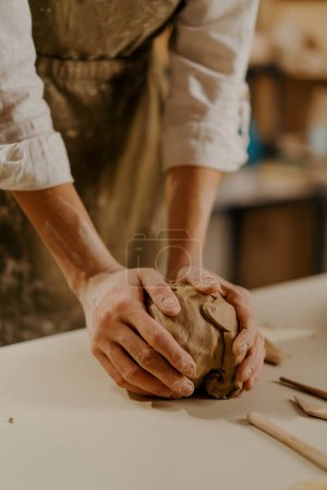 Foto de Taller de cerámica maestro amasa arcilla con sus manos en la mesa entre herramientas - Imagen libre de derechos