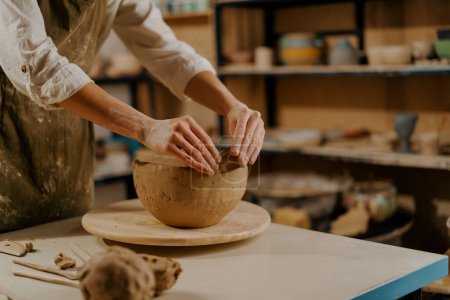 In the pottery workshop the master sculpts clay dishes with his hands on table