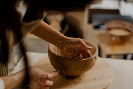 Téléchargez les photos : Dans l'atelier de poterie, le maître traite le produit avec une boucle pour l'argile sculpte des plats d'argile sur la table - en image libre de droit