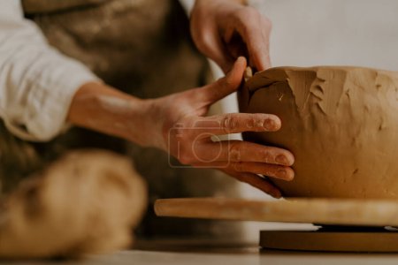 Photo for In the pottery workshop the master sculpts clay dishes with his hands on table - Royalty Free Image