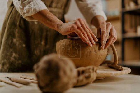 Foto de En el taller de cerámica el maestro esculpe platos de barro con las manos sobre la mesa - Imagen libre de derechos