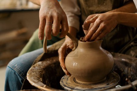 Foto de Taller de cerámica un alfarero enseña a un estudiante a esculpir una jarra de barro esculpir mango para jarra - Imagen libre de derechos