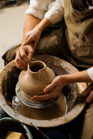 Téléchargez les photos : Atelier de poterie un potier enseigne à l'élève à sculpter cruche de couple d'argile est engagé dans la poterie - en image libre de droit