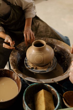 Téléchargez les photos : Un potier dans un atelier de poterie enlève une cruche de la roue du potier avec un couteau de potier - en image libre de droit