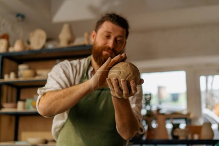 Téléchargez les photos : Atelier de poterie Un potier satisfait examine l'argile avant de commencer les travaux - en image libre de droit