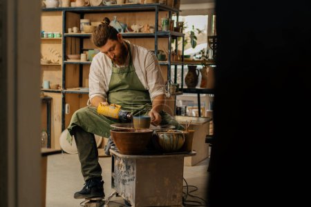 Téléchargez les photos : Un potier sèche une cruche peinte avec sèche-linge dans un atelier de poterie - en image libre de droit