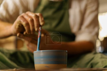 Téléchargez les photos : Poterie atelier potier peint cruche avec pinceau et peinture sur la roue du potier - en image libre de droit