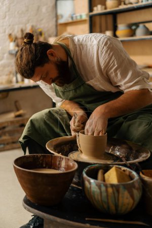 Foto de Un alfarero esculpe jarra en rueda de alfarero en taller de cerámica - Imagen libre de derechos