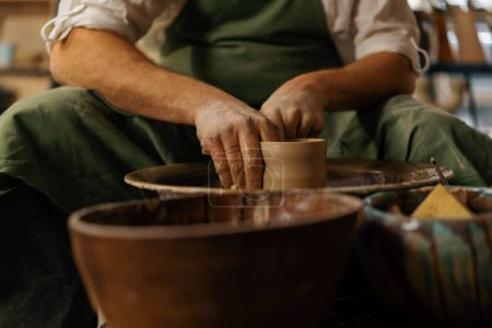 Téléchargez les photos : Un potier sculpte une cruche sur la roue du potier dans un atelier de poterie - en image libre de droit