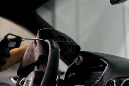 Photo for A mechanic in gloves cleans the steering wheel with microfiber cloth and blows dust with special tool - Royalty Free Image