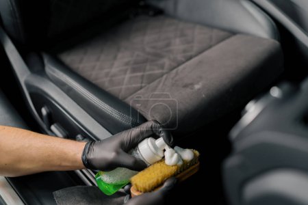 Téléchargez les photos : Nettoyage de l'intérieur de la voiture avec une brosse Une voiture détaillant travailleur nettoyage intérieur de la voiture et siège avec brosse et mousse le concept de détails de voiture - en image libre de droit