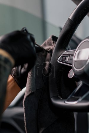 Photo for A mechanic in gloves cleans the steering wheel with microfiber cloth and blows dust with special tool - Royalty Free Image