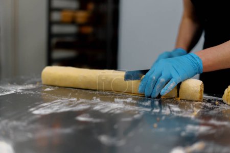 Téléchargez les photos : La cuisine dans la boulangerie - le processus de fabrication de cannons, la boulangerie femme coupe la pâte - en image libre de droit